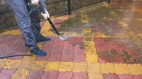 A man cleans the tile on the sidewalk from the build up of dirt. Stock-Footage 128075568