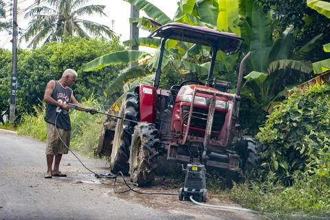 A man cleans a tractor using a stream of water on a village road Stock Photos