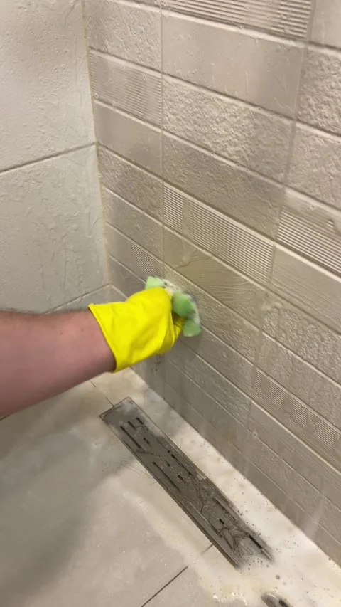 Man cleans wall with ceramic tiles, drain, floor with yellow coating Stock Footage 308923094