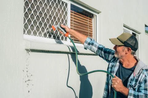 Man cleans window with flow of water by hose pipe Stock Photos