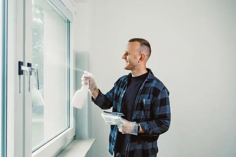 Man cleans window with spray and cloth in bright room during day in home im.. 写真素材