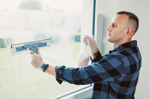Man cleans window with a squeegee during a bright afternoon in a modern roo.. Stock Photos