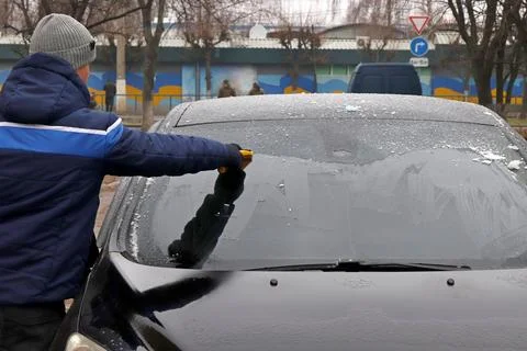 A man cleans the windshield of a car with a scraper. Foto stock