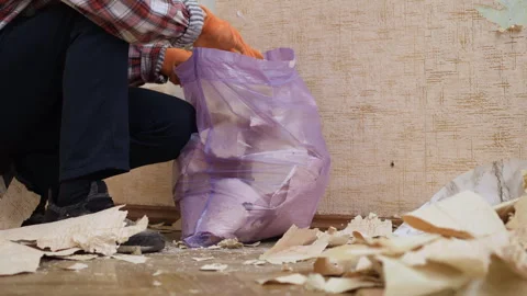 Man clearing construction waste and old wallpaper into a trash bag, preparing Stock Footage 329757184