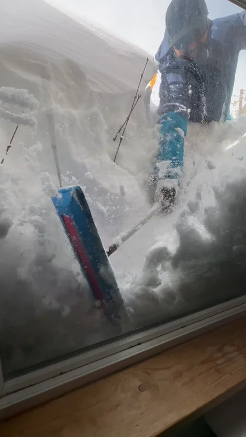 Man clearing snow from window of buried home in Tahoe after blizzard Stock Footage 261934182