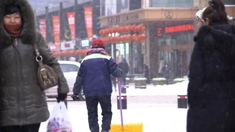 Man clearing thick snow as people walking by in light snowfall, China, Shenyang 스톡 동영상 84699658