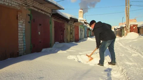 A man clears the passage to the garage from snow with a wooden shovel. Stock Footage 224680334