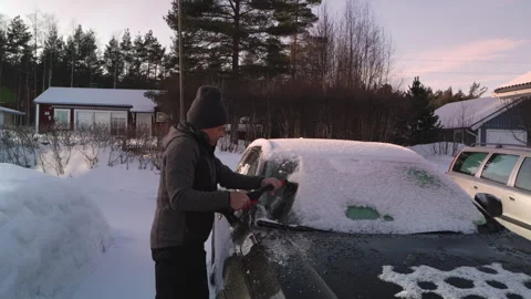 A man clears snow and ice from his car windshield using a snow brush during.. Stock Footage 287078071