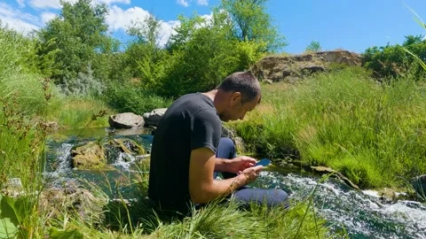 A man clicking or playing on the smart phone by the river 库存影片 199191762
