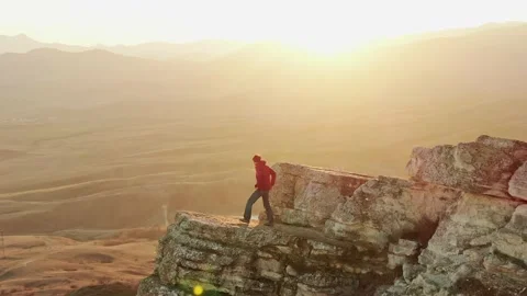 A man climbed a cliff ledge and watches the sunset in the bright sunbeams in the Stock Footage 150566315