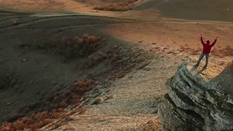 A man climbed a rock ledge and watches the sunset in bright sunlight. Aerial vie Stock Footage 150566270
