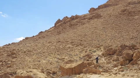 Man climbing with backpack and sticks on rocky desert mountain on sunny day Видео 330301248
