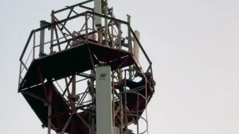 Man Climbing Mobile Tower in Rural Area Highlighting Dangerous Risk 库存影片 323103624