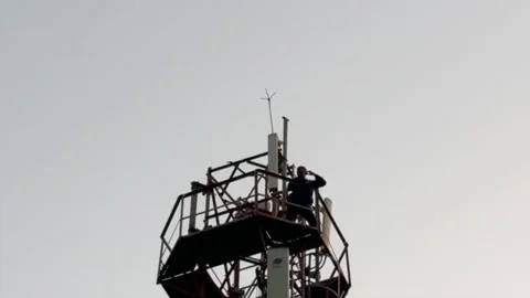 Man Climbing Mobile Tower in Rural Area Highlighting Dangerous Risk Stockbeeldmateriaal 323103638