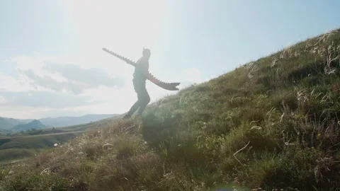 A man climbs a hillside with a feather-grass and carries a Didgeridoo on his Stock-Footage 244990695