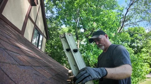 Man climbs ladder to clean gutters on his house Stock Footage 337603877