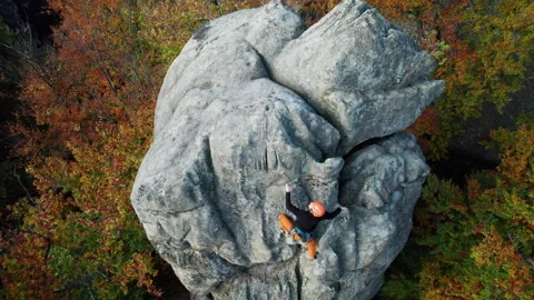Man climbs natural sandstone face in autumn woodland, wearing harness and safety Stock Footage 346546084
