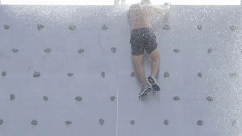Man climbs over rock wall obstacle course with water Stock Footage 73055159