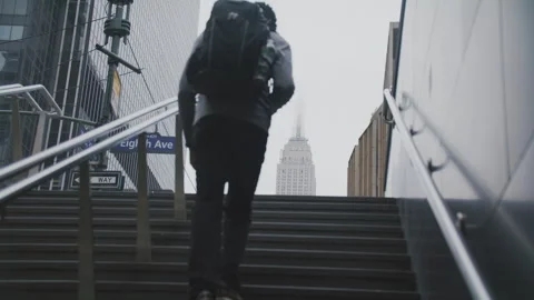Man climbs stairs with backpack towards iconic skyscraper in urban setting Stock Footage 312591150