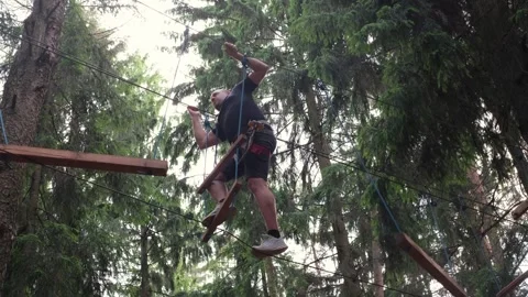 A man climbs a suspension bridge at a height between trees Stock Footage 337183339