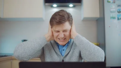 A man closes his ears while sitting at the computer at home Stock Footage 148344416