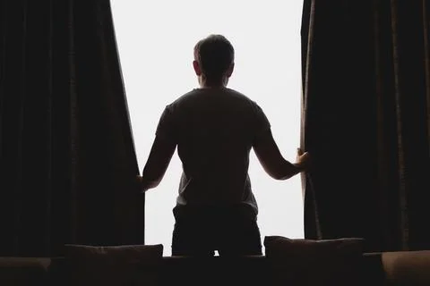 Man closing the curtain while watching the view out of the window. Foto stock