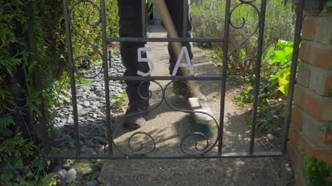 Man closing a gate and sweeping a garden path. Video stock 139451362