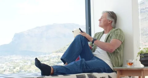 Man is closing strapped notebook on window bench, lifting head and watching Stock Footage 339591713