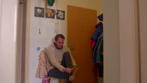 A man in a coat reflects while tying his shoes in a quiet hallway Stock Footage 311205291