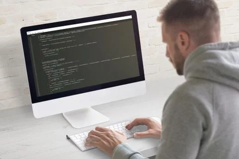 Man coding app on a computer. Close-up scene. Clean office desk with brick wa Stock Photos