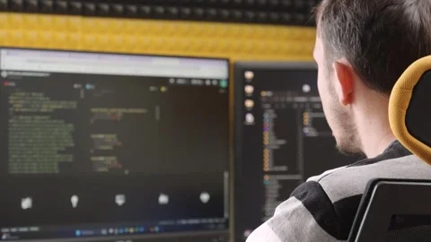 Man coding on dual monitors in soundproof workspace, focused on programming Stock Footage 309313068
