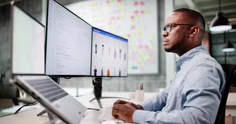 Man Coding Ecommerce Software On Multiple Monitors In Office Chair Foto stock