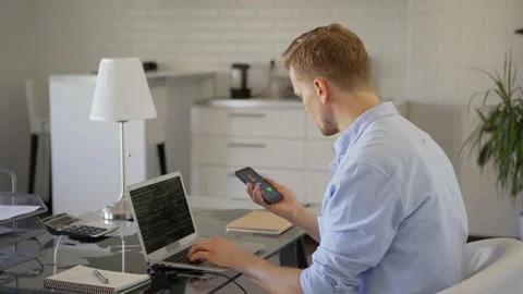 Man coding on laptop and discussing work on phone Stock Footage 133956432