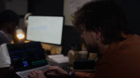 Man Coding on Laptop with Diverse Colleague Working Late in Office Stock Footage 338417672