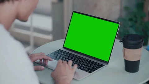 Man coding on laptop with green screen at outdoor table using coffee cup nearby Stock Footage 340843688