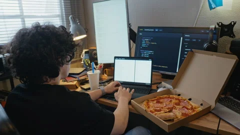 Man Coding Software on Laptop with Pizza on Desk at Home Stock Footage 338423386
