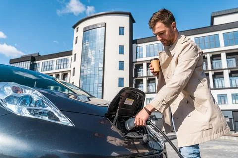 Man with coffee cup in hand inserts plug into the charging socket Stock Photos
