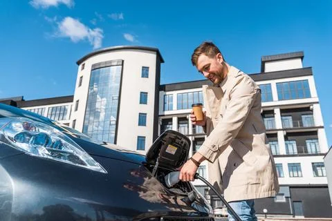 Man with coffee cup in hand inserts plug into the charging socket Stock Photos