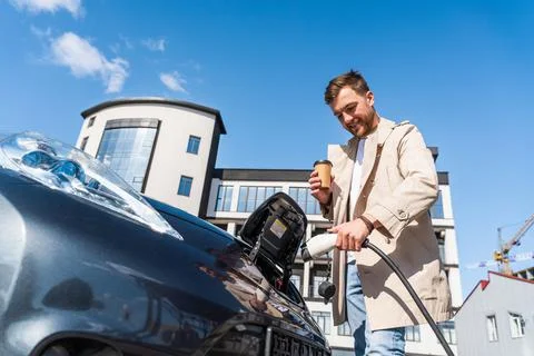 Man with coffee cup in hand inserts plug into the charging socket Stock Photos