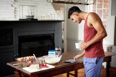Man with coffee cup using tablet computer while standing by table in kitchen Stock-Fotos