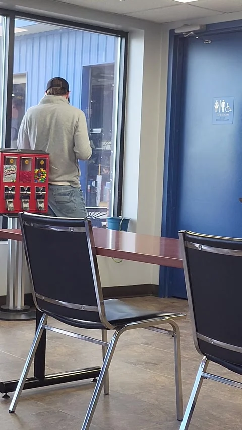 Man with coffee talks on cell phone looking out window waiting in a break room Stock Footage 340236939