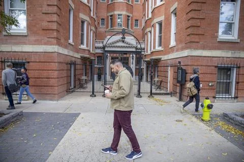 Man with coffee using smart phone, walking outside brick apartment building Stock Photos