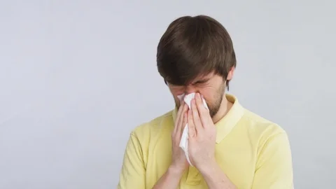 Man with cold blows his nose into tissue wearing yellow shirt isolated on grey Stock Footage 127102914