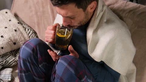A man with a cold drinks tea and coughs while sitting on the sofa Видео 331261509