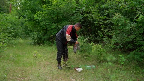 Man collect garbage in forest in bag. Young adult attractive male volunteer Stock Footage 158124433