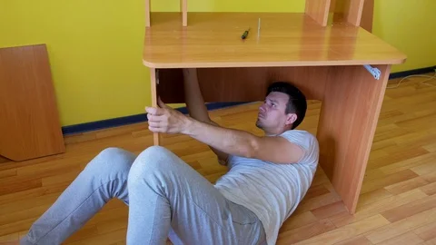 Man collecting parts of computer table screwing with bolts lying under table. Stock Footage 125040533