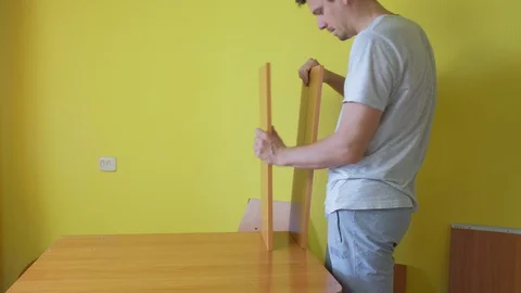Man is collecting parts of computer table on yellow wall background. Stock Footage 129420841