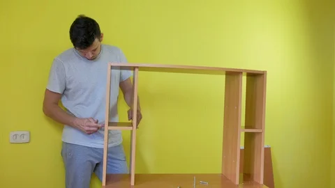 Man is collecting parts of computer table screwing shelf using screwdriver. Stock Footage 129423468