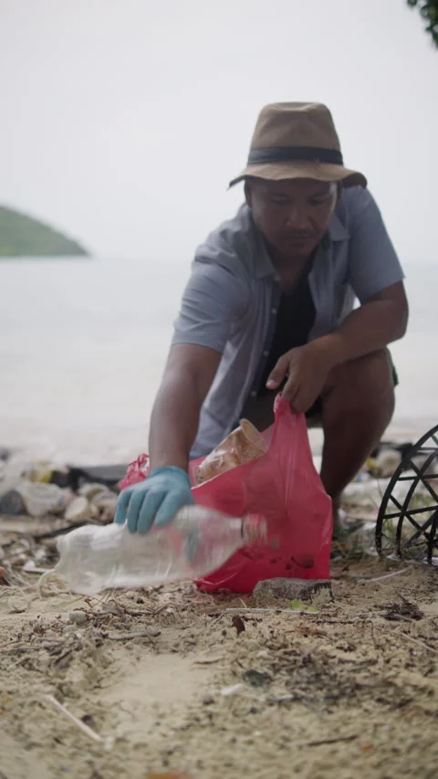 A man collecting plastic trash from a polluted beach, environmental awareness 動画素材 343574188
