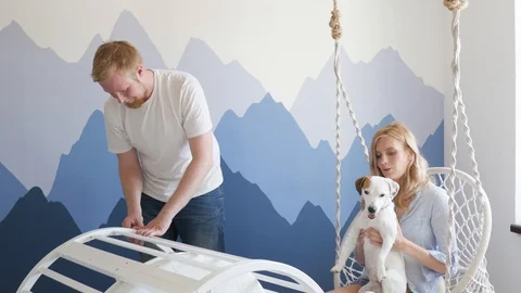 A man collects a crib for a child, his wife plays with a dog Jack Russell Video stock 118632016